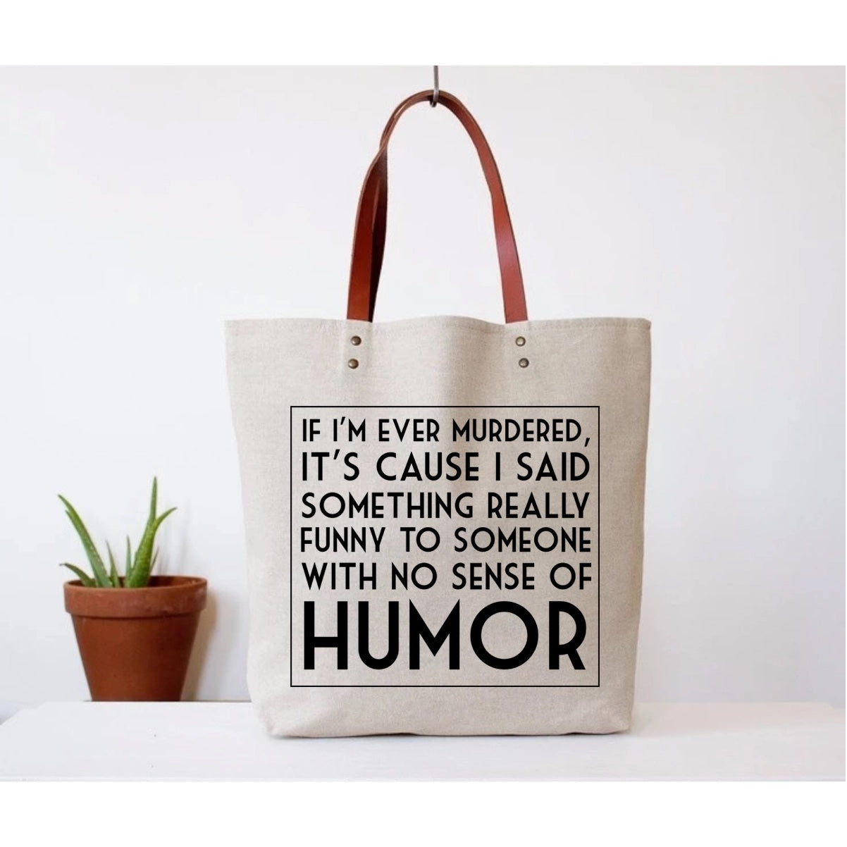 Canvas tote bag with faux leather straps that says "If I'm ever murdered t's cause I said something funny to someone with no sense of humor"